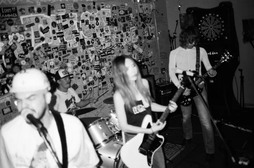 Ant Airdo, Donovan Ryan, Rose Thorne and Nate VanDerPol playing in front of the sticker wall